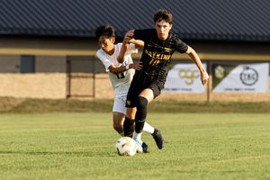 Two soccer players compete for possession of the ball during a match on a grass field at sunset.