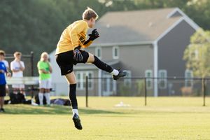 Ultimate frisbee player leaps high into the air to make a catch on a sunny grass field during a match.