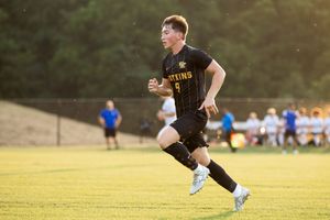 Soccer players in black uniforms practice on a grass field during golden hour.
