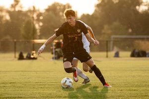 Soccer player dribbles ball on grass field during golden sunset practice session.