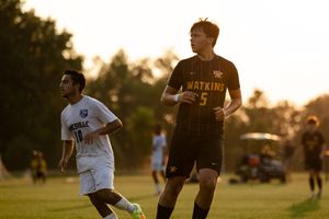 Soccer players compete for the ball during a match at sunset on a grass field.