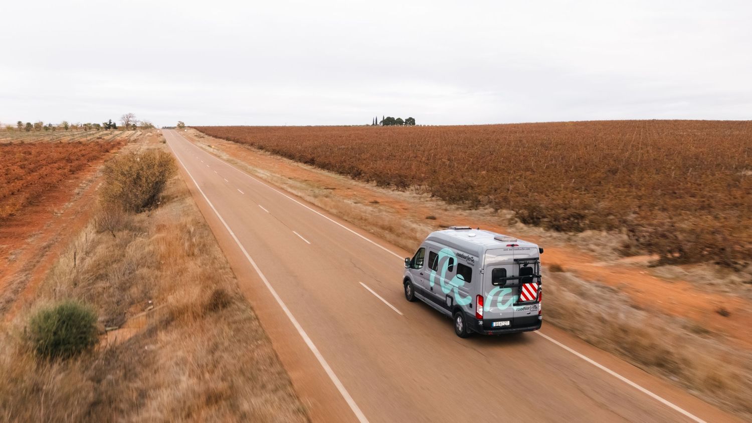Aerial panorama of a camper van driving along a remote desert highway.