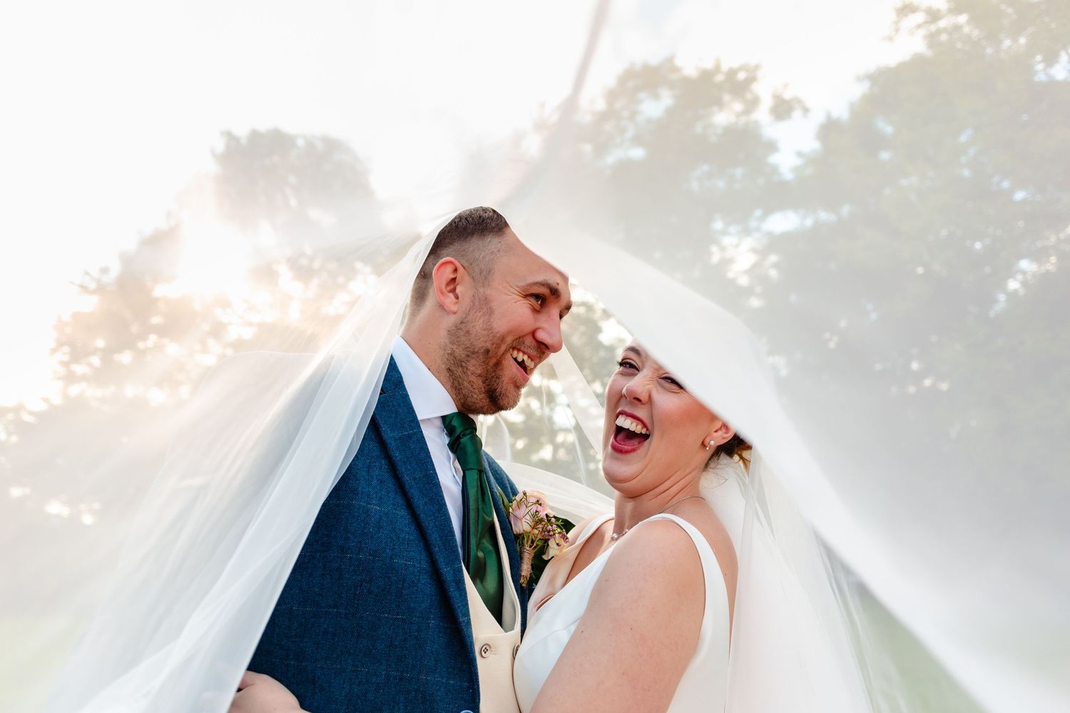 Bride and groom embracing each other under the bride's veil, laughing at the camera, at Washingboorugh Hall, Lincoln.