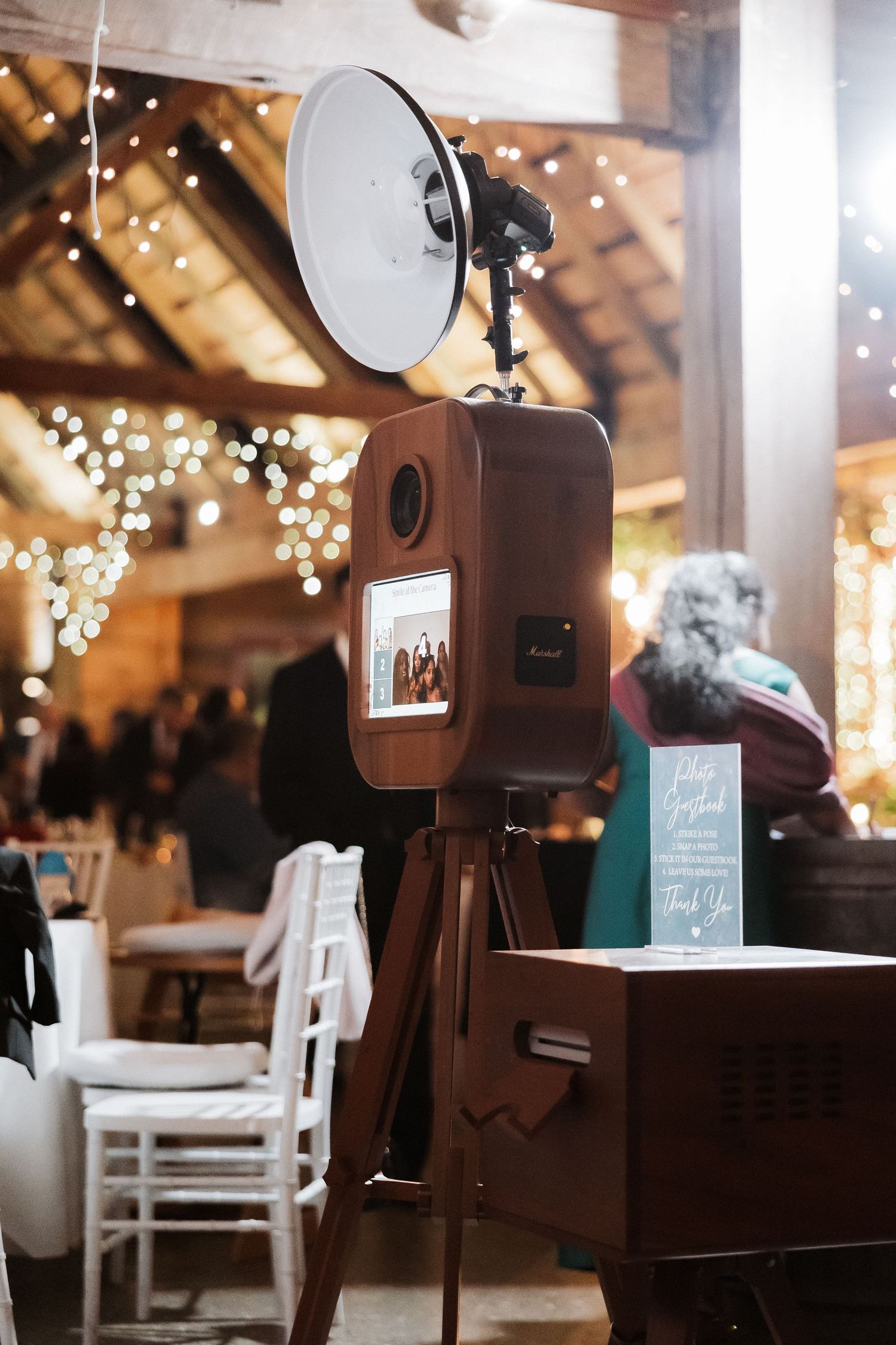 Photo booth setup with vintage camera equipment at a rustic wedding venue decorated with twinkling string lights.