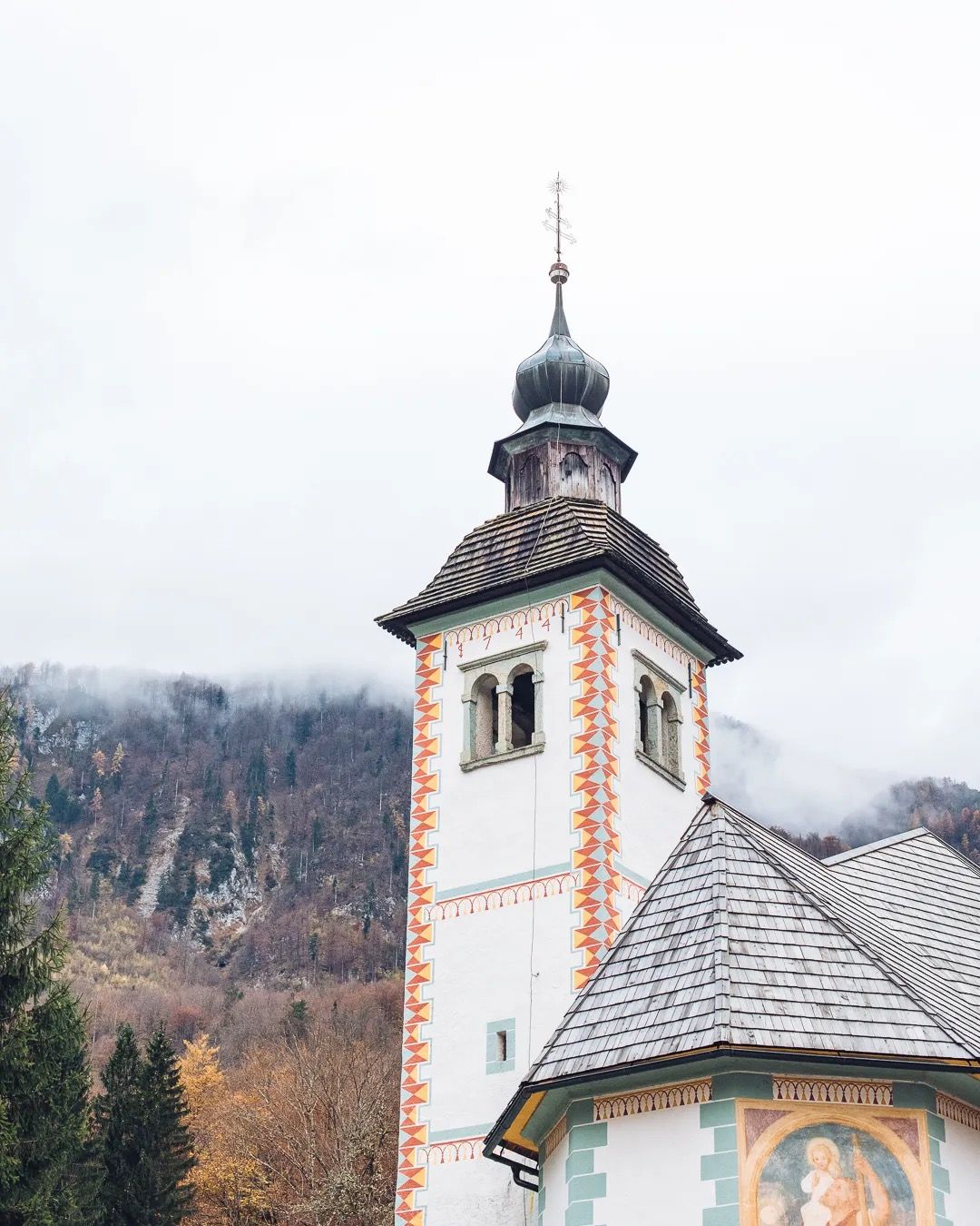 Picturesque Alpine church tower surrounded by mountains on a soft misty day.