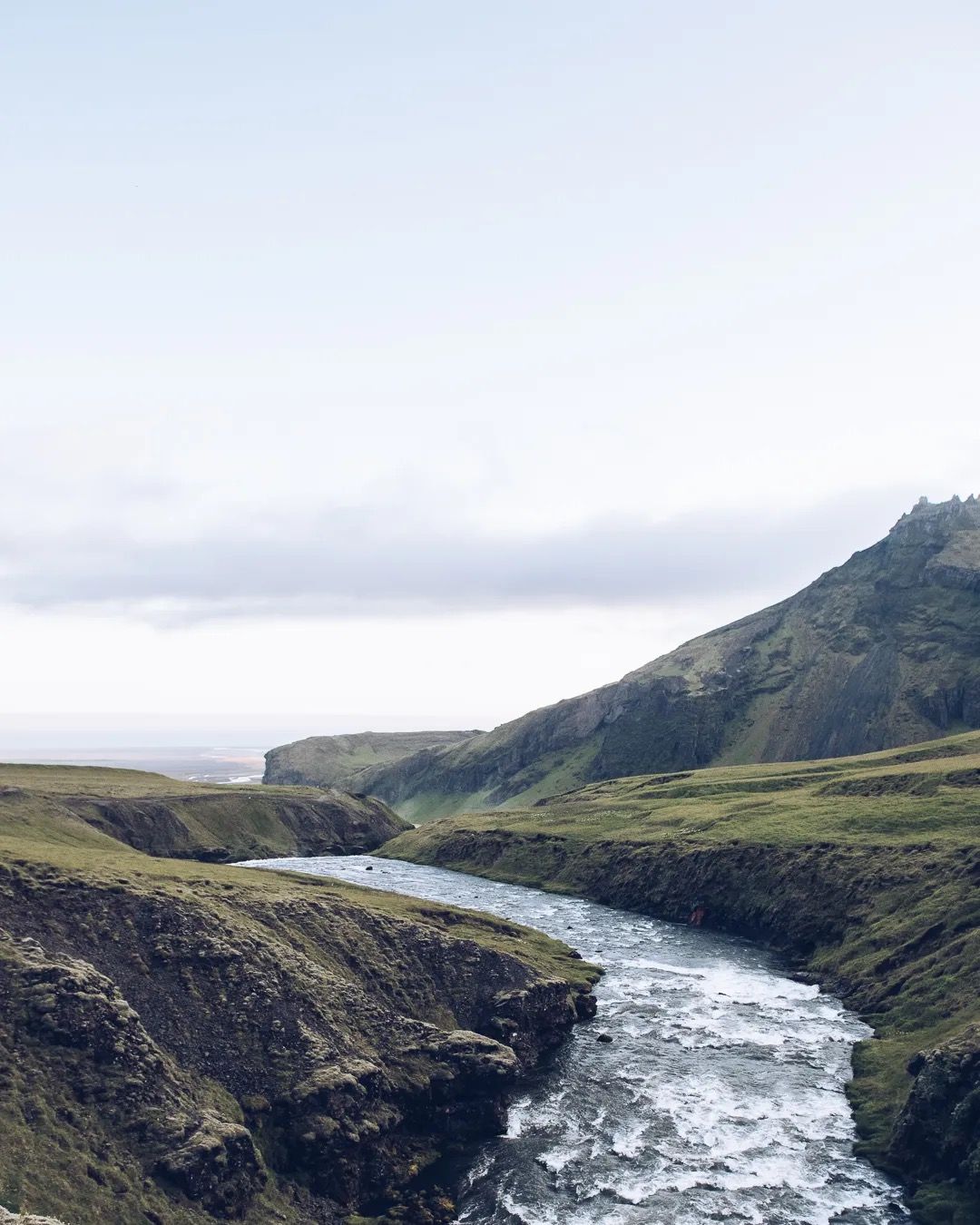 Mountain river cutting through a steep Icelandic gorge on a bright day.