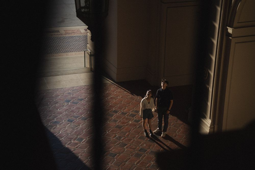 Cinematic wide shot of couple framed beneath grand archway in Pasadena City Hall.