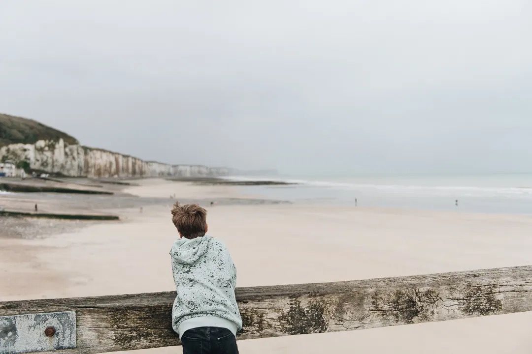 Child looking out over a wide sandy beach with cliffs on a cloudy day.