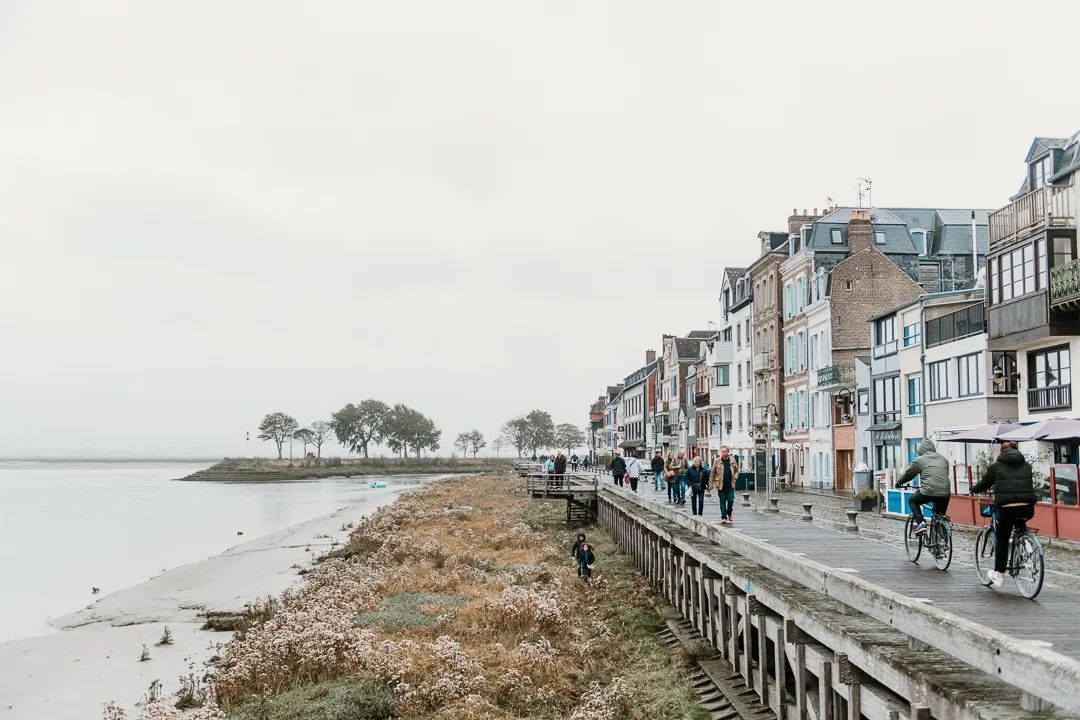 Coastal town walkway beside the shoreline with people walking along a row of seaside buildings.