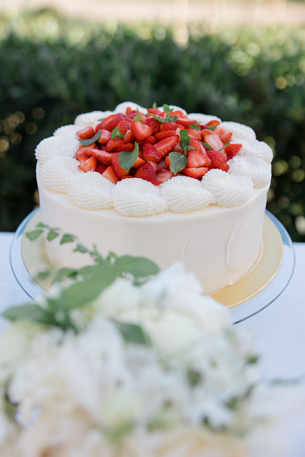 A series of white meringue pavlova desserts topped with fresh red strawberries and green eucalyptus leaves on display.