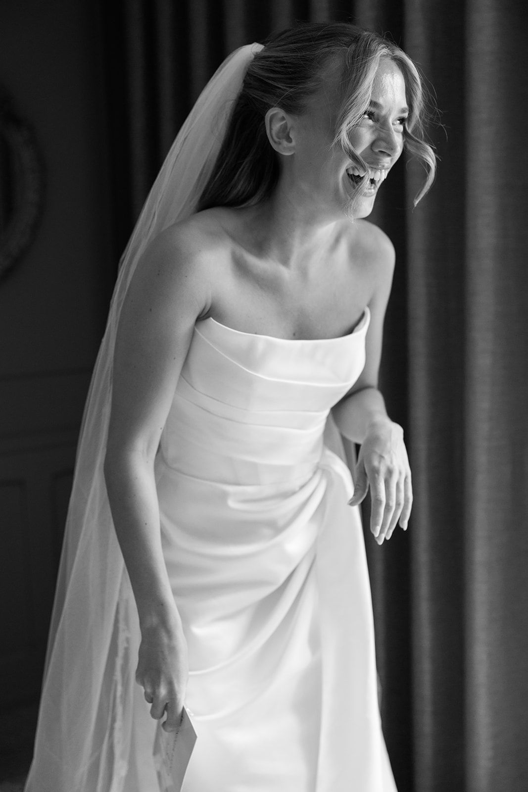A bride in a classic white strapless wedding gown and veil stands elegantly in a black and white portrait series.