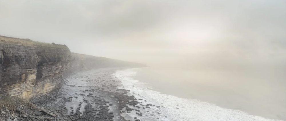 Misty coastal landscape with dramatic cliffs and rocky shoreline stretching into the distance.