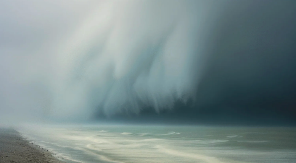 Dramatic stormy seascape with dark moody clouds and misty atmosphere over a coastal shoreline.