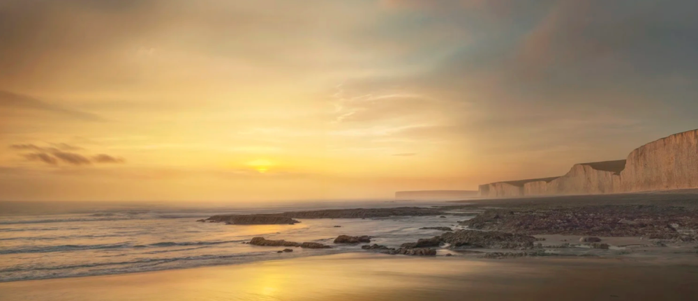 Golden sunset illuminates white cliffs along a serene beach coastline.