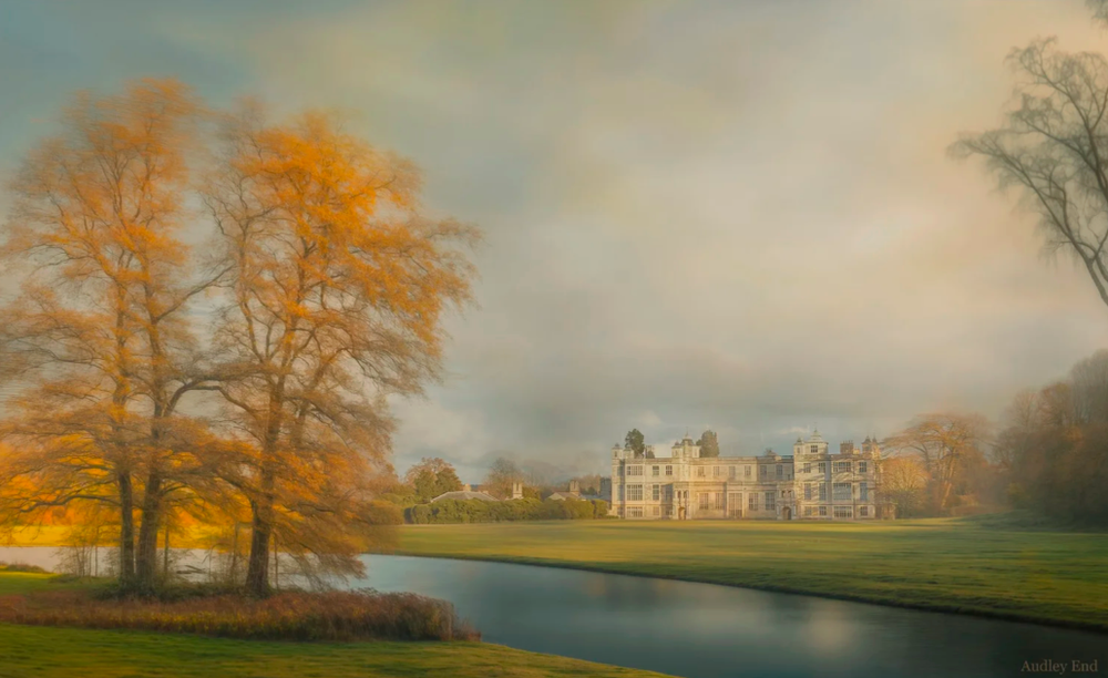 Majestic mansion reflected in a lake surrounded by autumn trees with golden foliage.