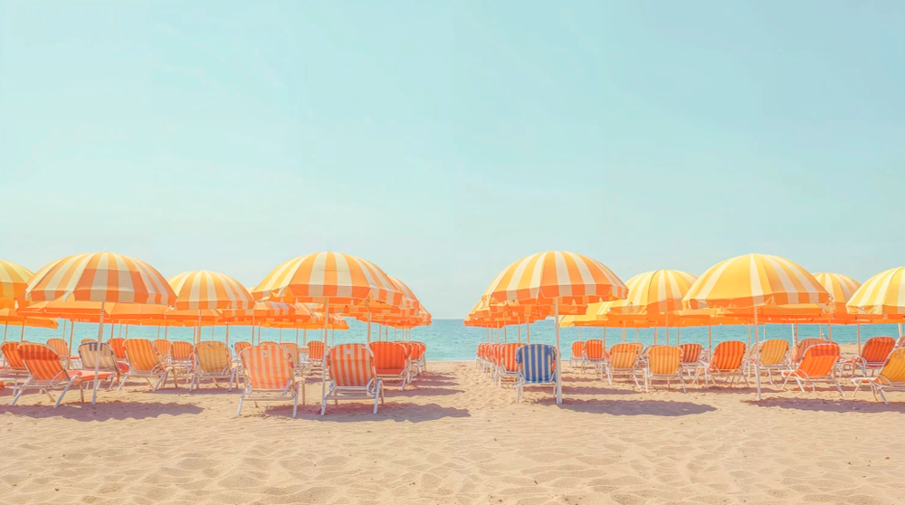 Row of bright orange beach umbrellas and lounge chairs on a sandy beach.