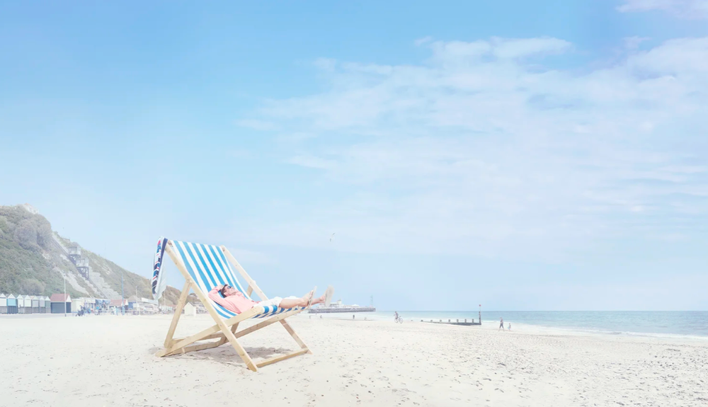 Minimalist beach scene with striped deck chairs on white sand against blue sky.