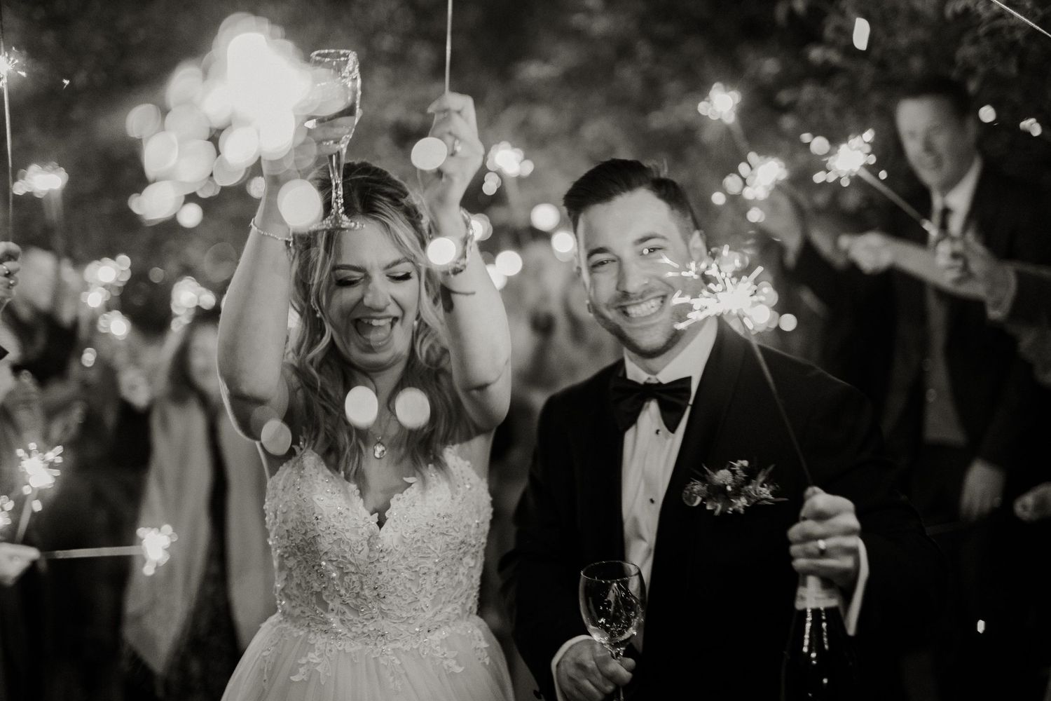 Black and white photo of newlyweds celebrating with sparklers at nighttime reception.