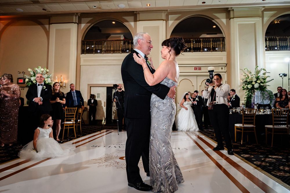 A couple shares an intimate dance in a grand ballroom with elegant decor and arched details.