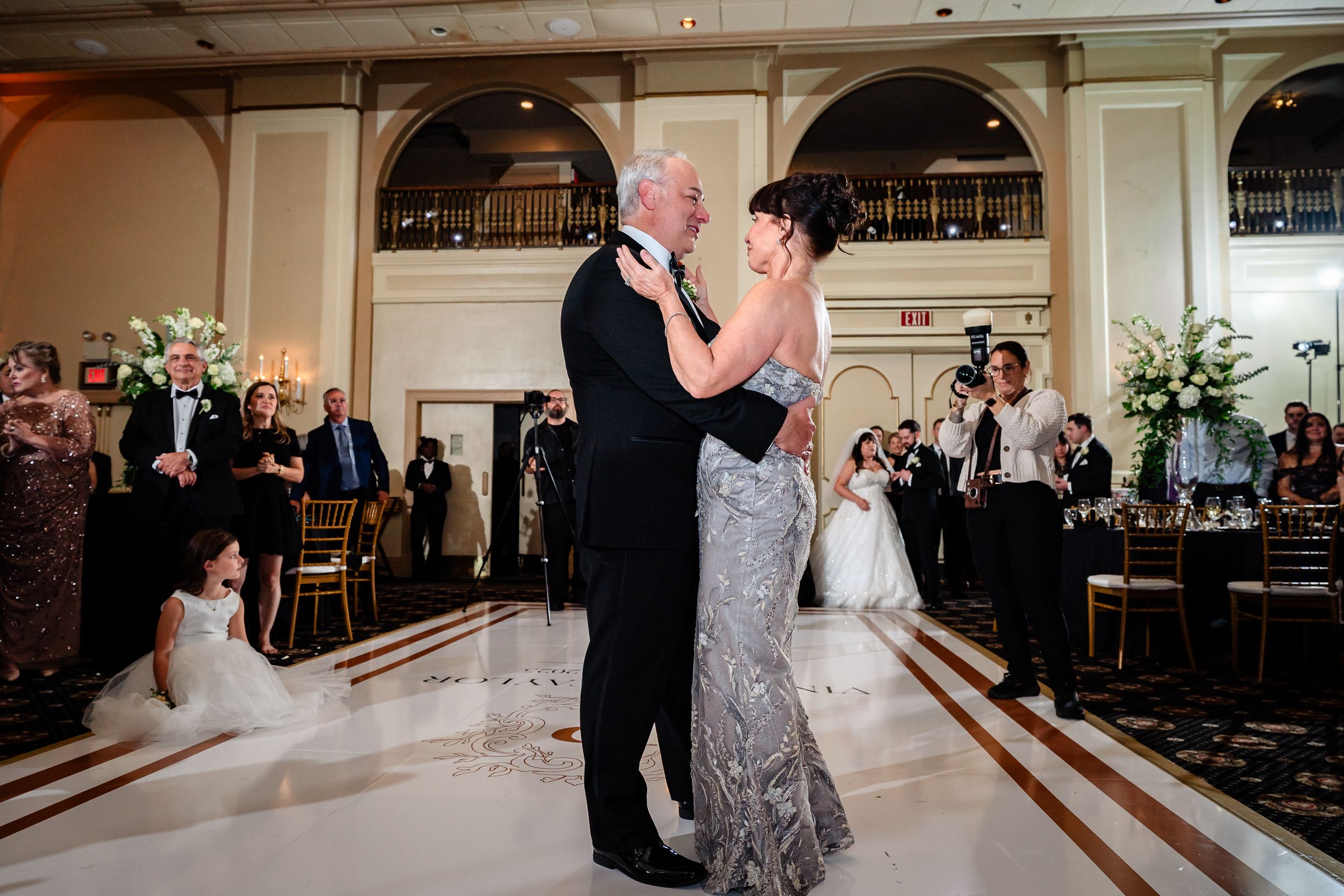 A couple shares an intimate dance in a grand ballroom with elegant decor and arched details.