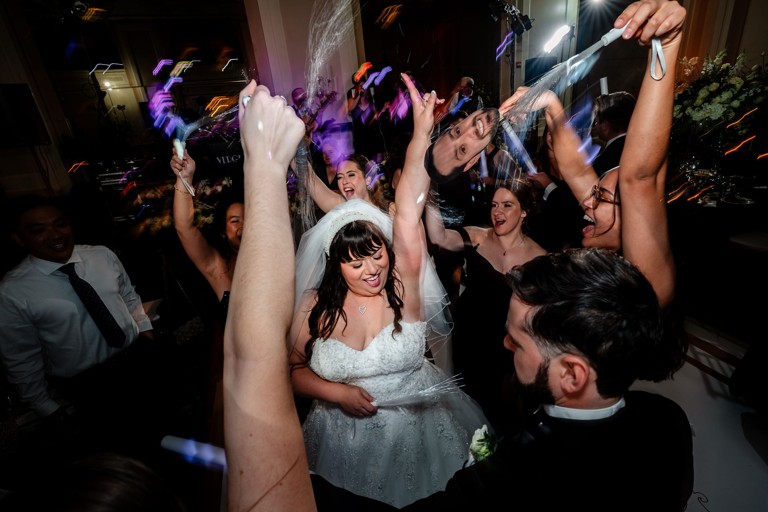Wedding party dancing and celebrating on a dimly lit dance floor during evening reception.
