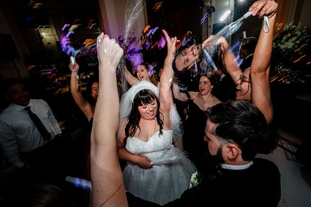 Wedding party dancing and celebrating on a dimly lit dance floor during evening reception.