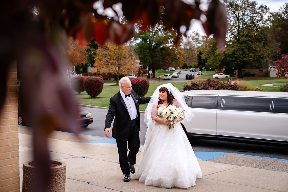 Wedding party walking along a stone pathway surrounded by autumn trees and landscaping.