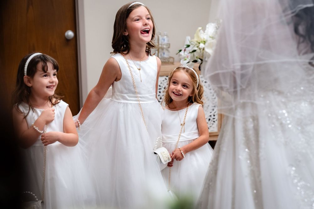Young attendants in white dresses react with excitement to seeing the bride.