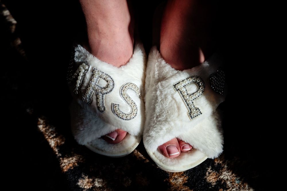 White fuzzy slippers with 'Mrs' text worn at a wedding celebration.