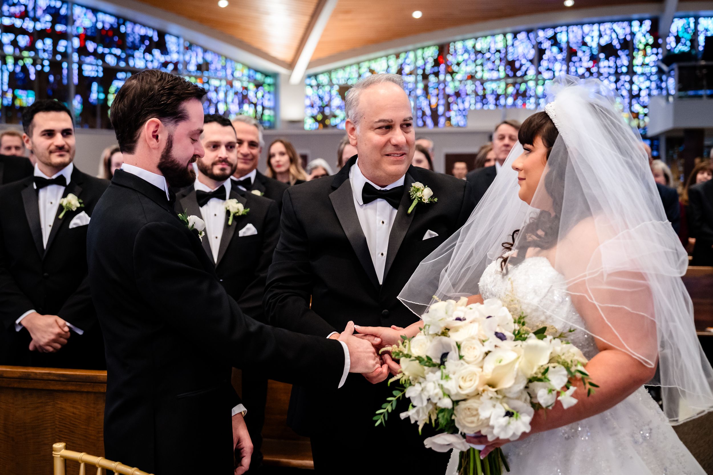 Wedding ceremony in church with stained glass windows and formal attire.