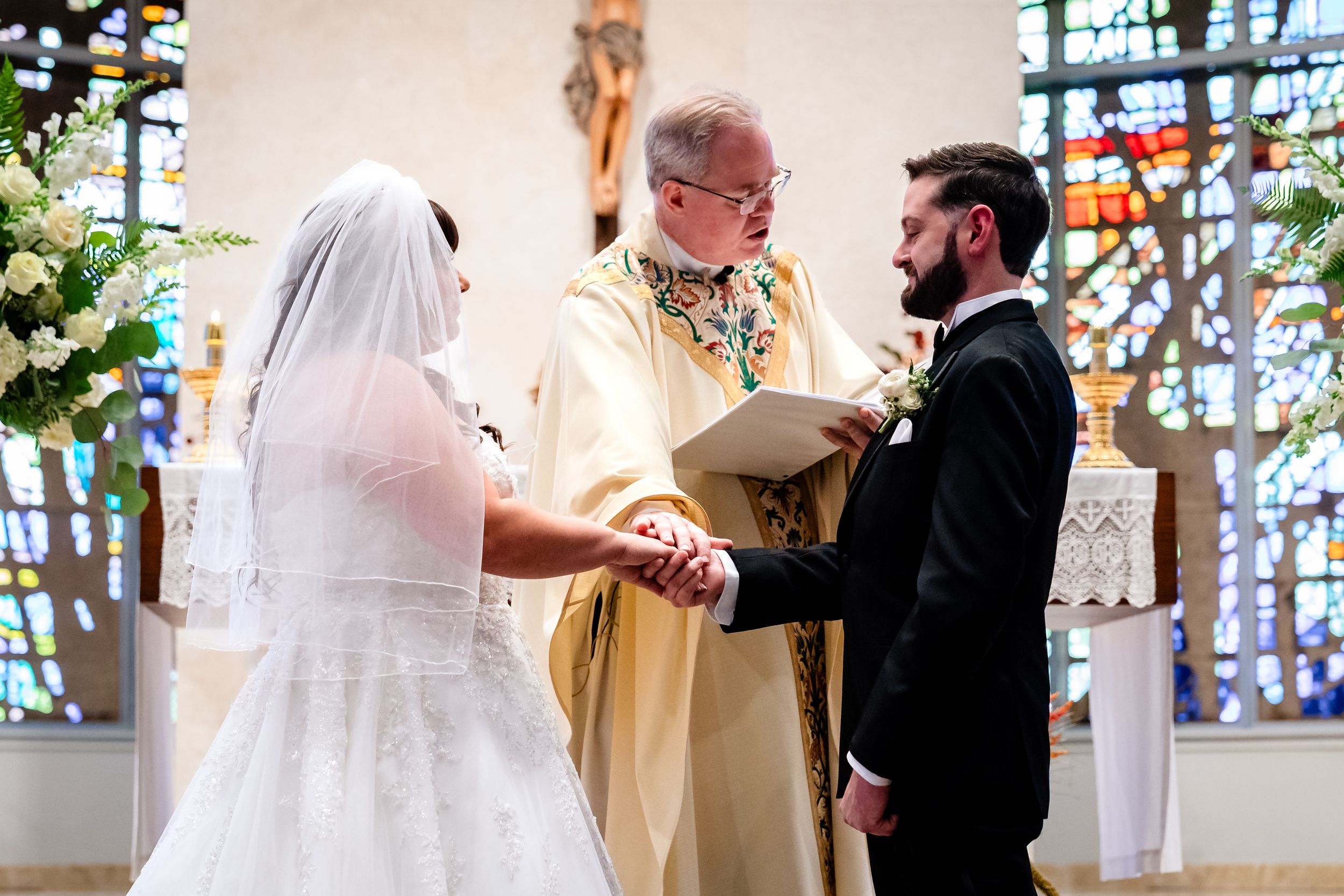 A wedding ceremony takes place in a beautiful church with stained glass windows.