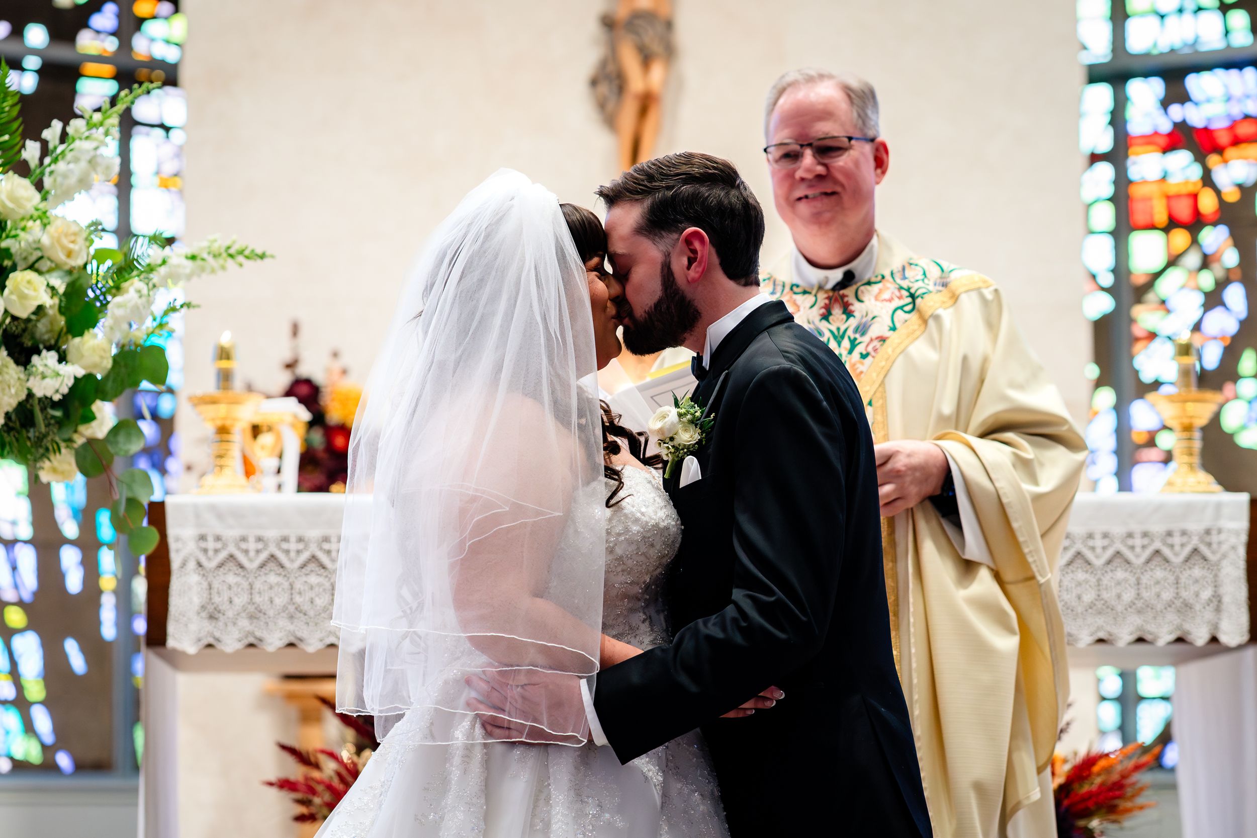 Wedding ceremony in a church with stained glass windows and traditional altar decorations.