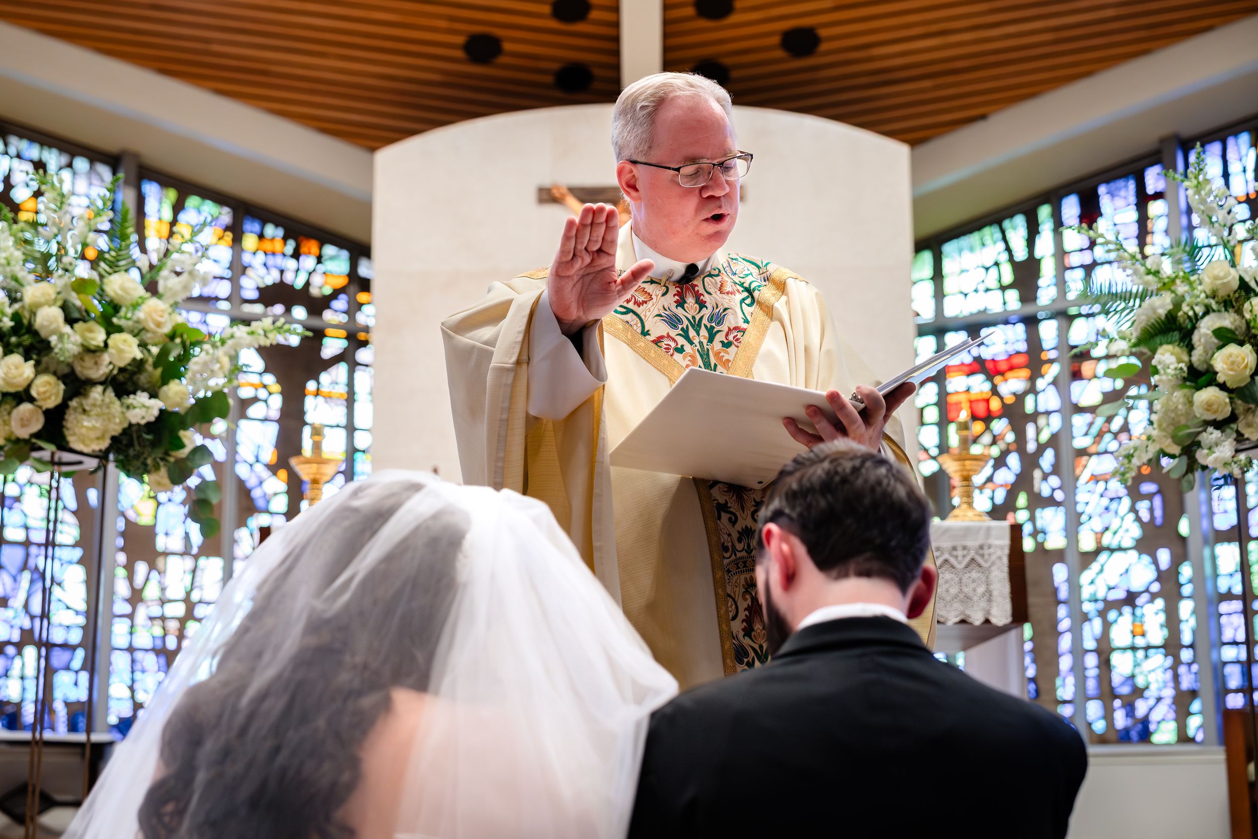 Traditional church wedding ceremony with wooden ceiling beams and colorful stained glass windows.