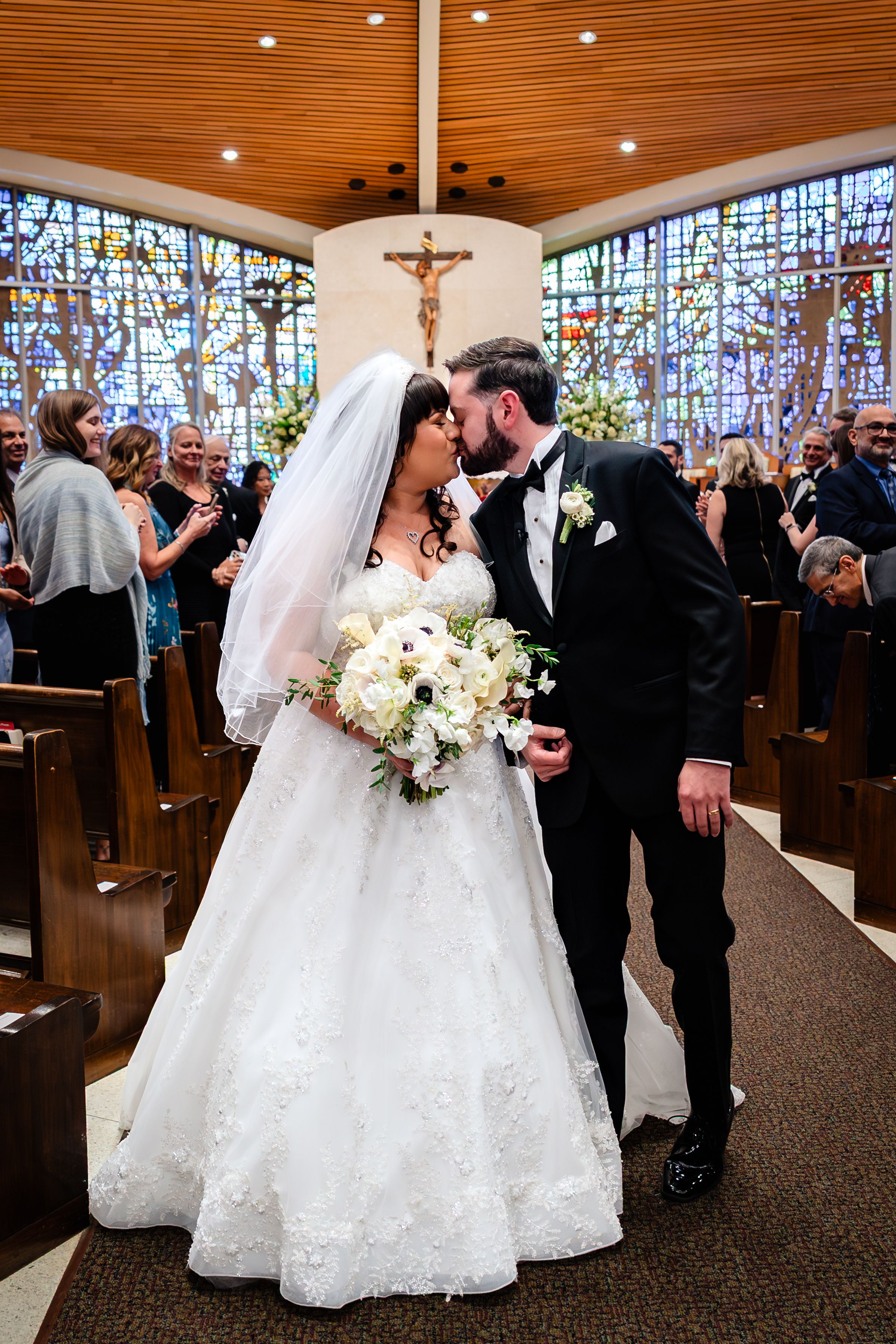 Wedding ceremony in church with stained glass windows and wooden ceiling details.