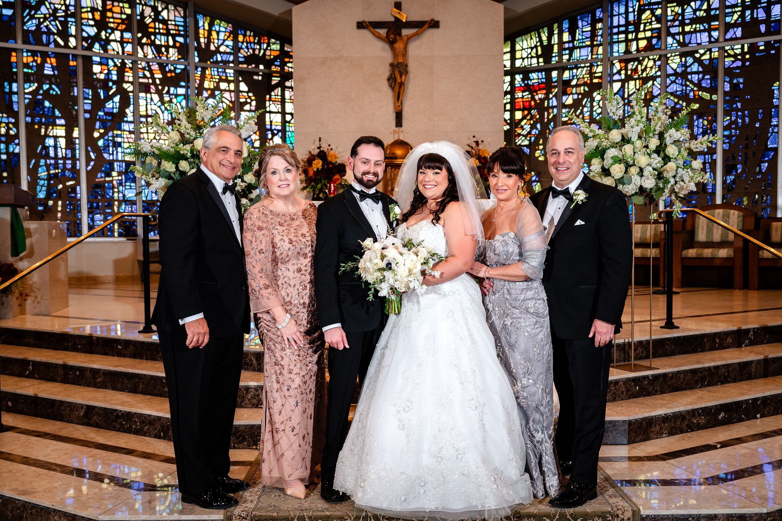Wedding ceremony in a church with stained glass windows and floral arrangements at the altar.