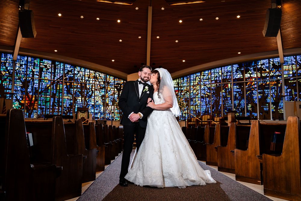 Newlyweds share a moment in a church with stunning blue stained glass windows behind them.