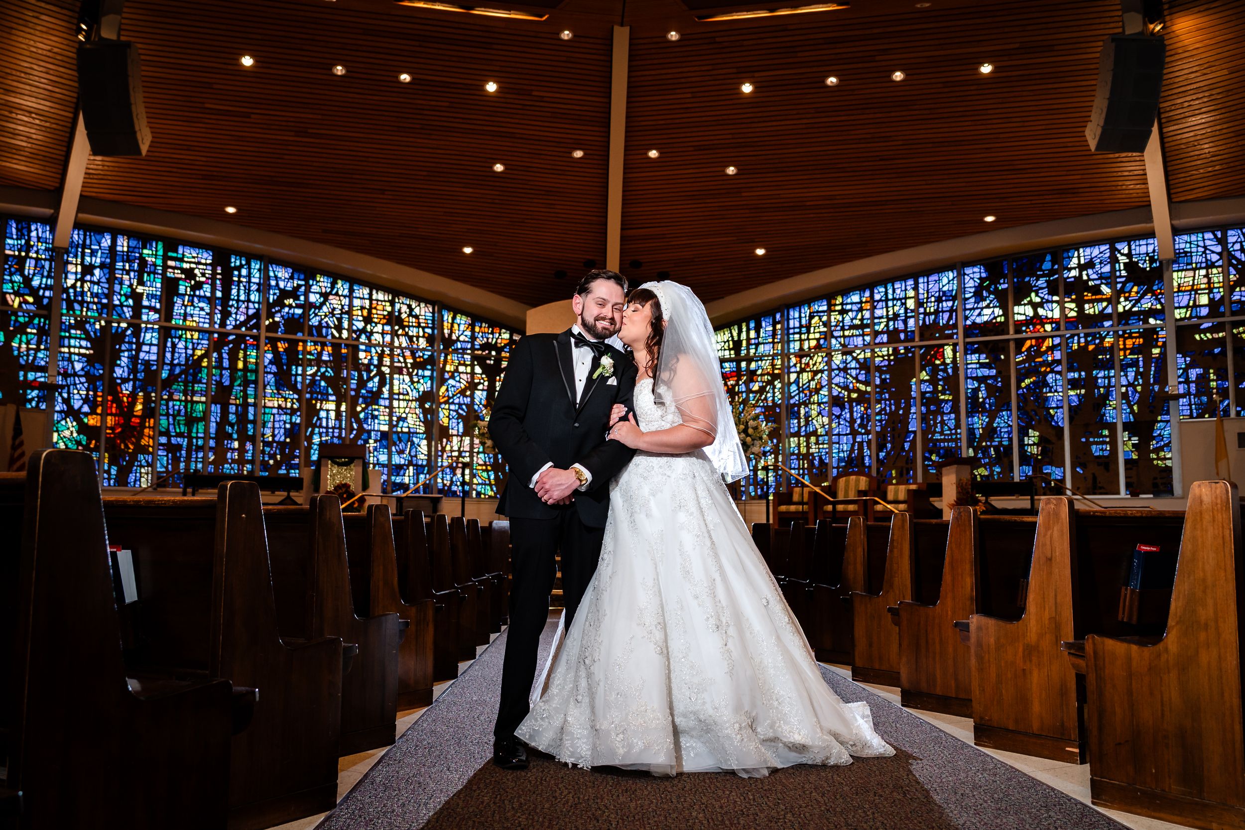 Newlyweds share a moment in a church with stunning blue stained glass windows behind them.