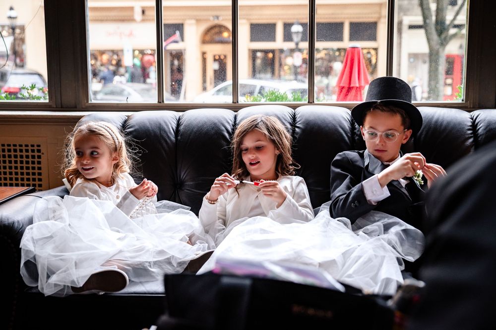 Babies in white outfits lie in a row on a bench by a window in a nursery setting.