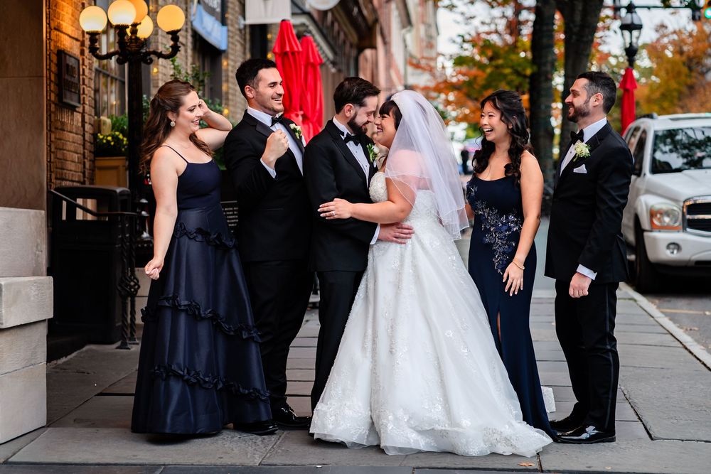 Wedding party in navy and white attire posing outside venue during autumn season.