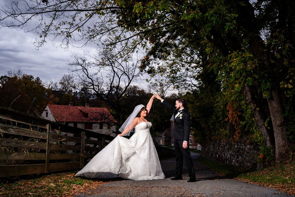 Wedding couple and party members posing along rustic wooden fence in autumn landscape.