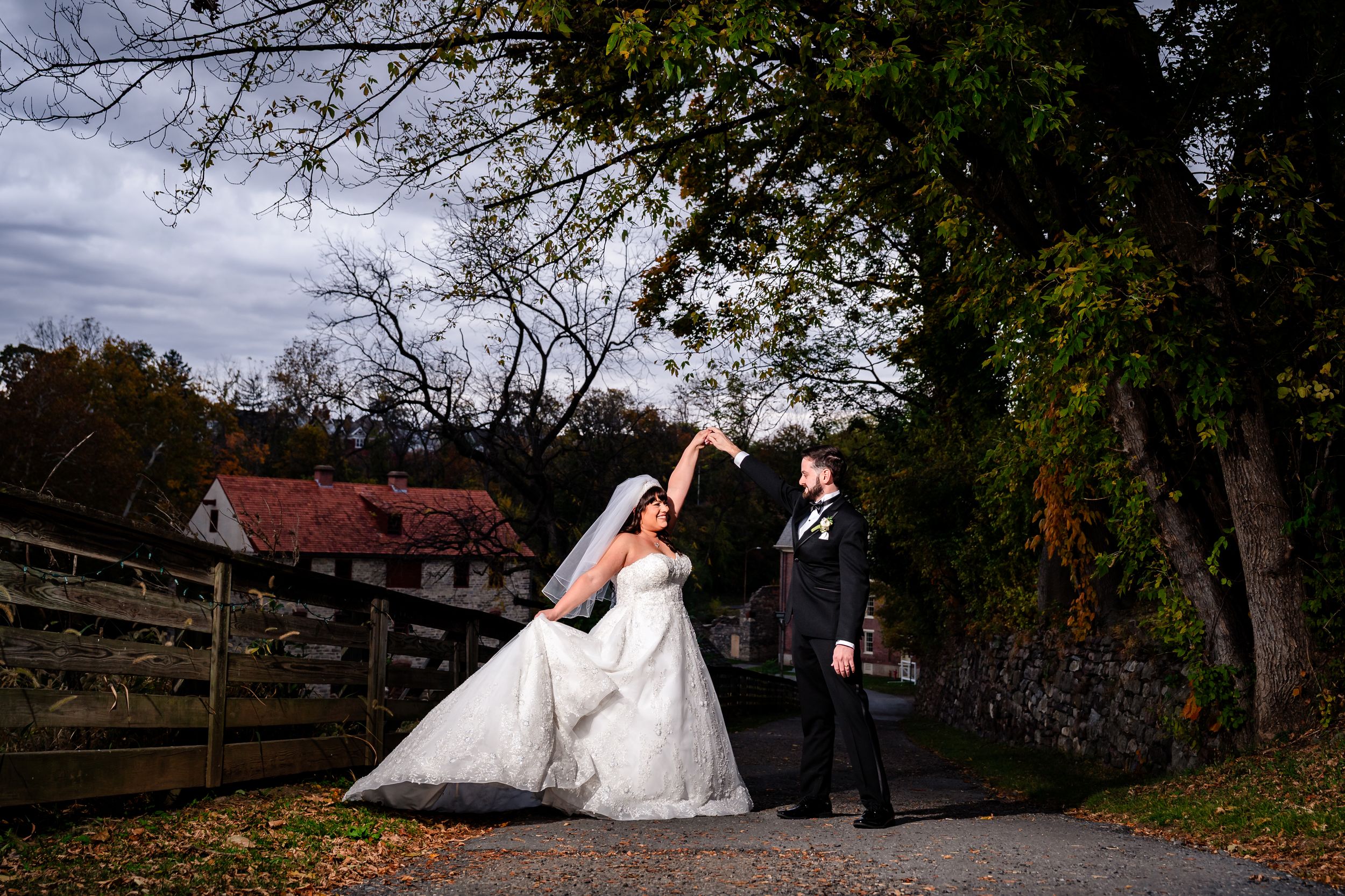 Wedding couple and party members posing along rustic wooden fence in autumn landscape.