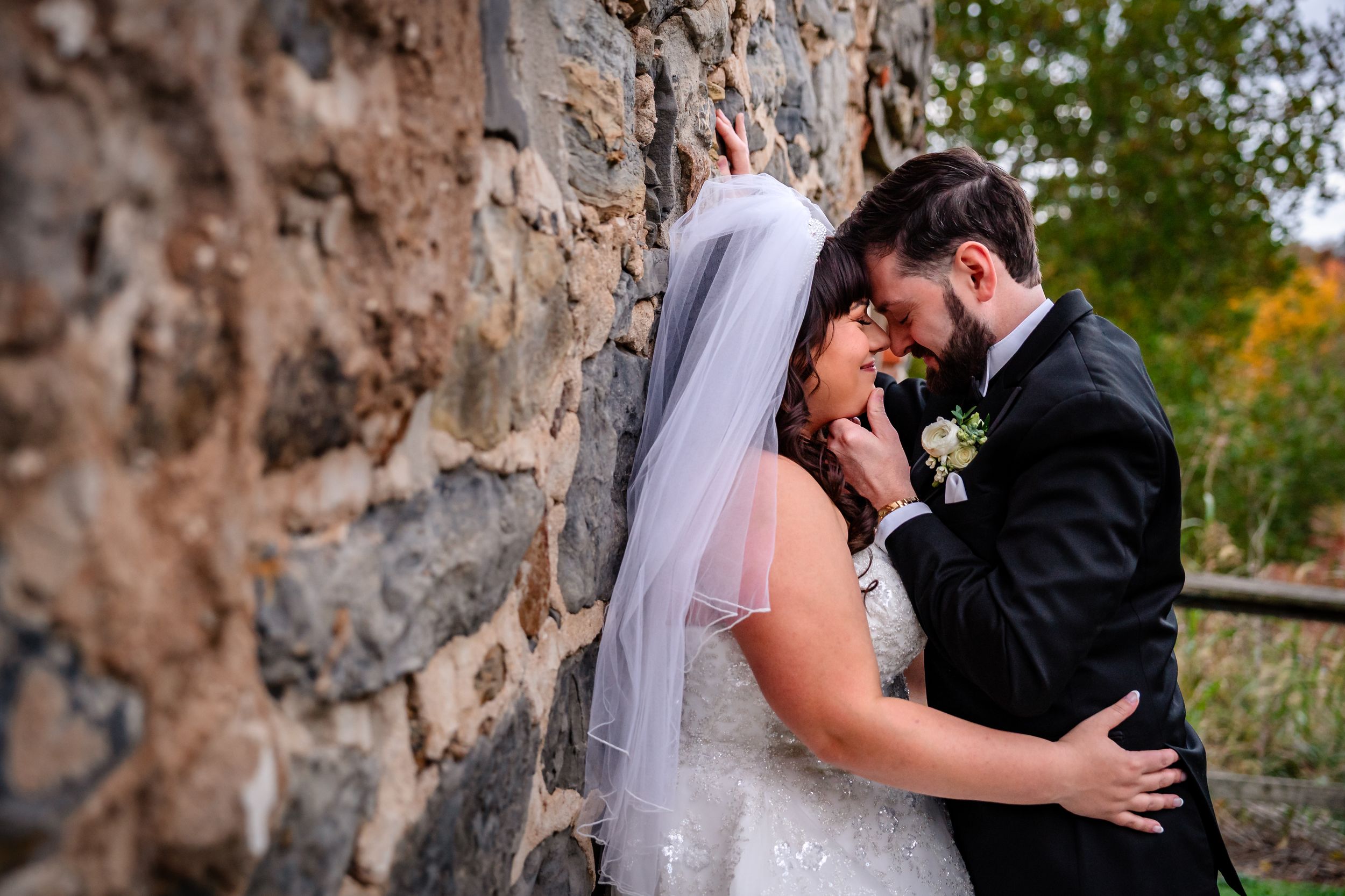 A romantic wedding moment captured against a rustic stone wall backdrop.