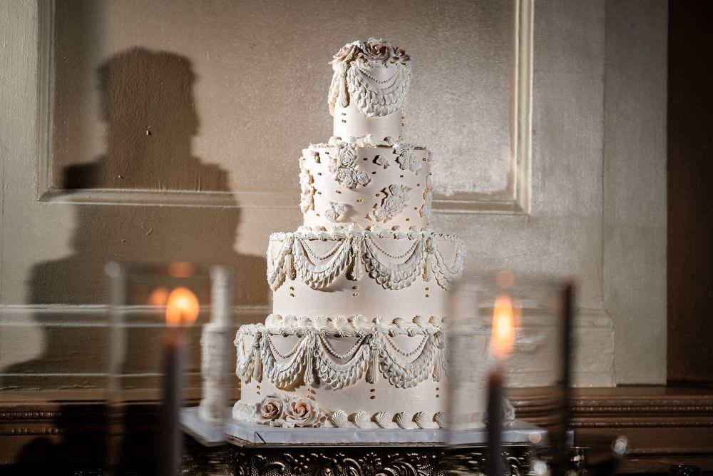 Ornate white wedding cake with delicate lace details and tiered design displayed in elegant reception setting.