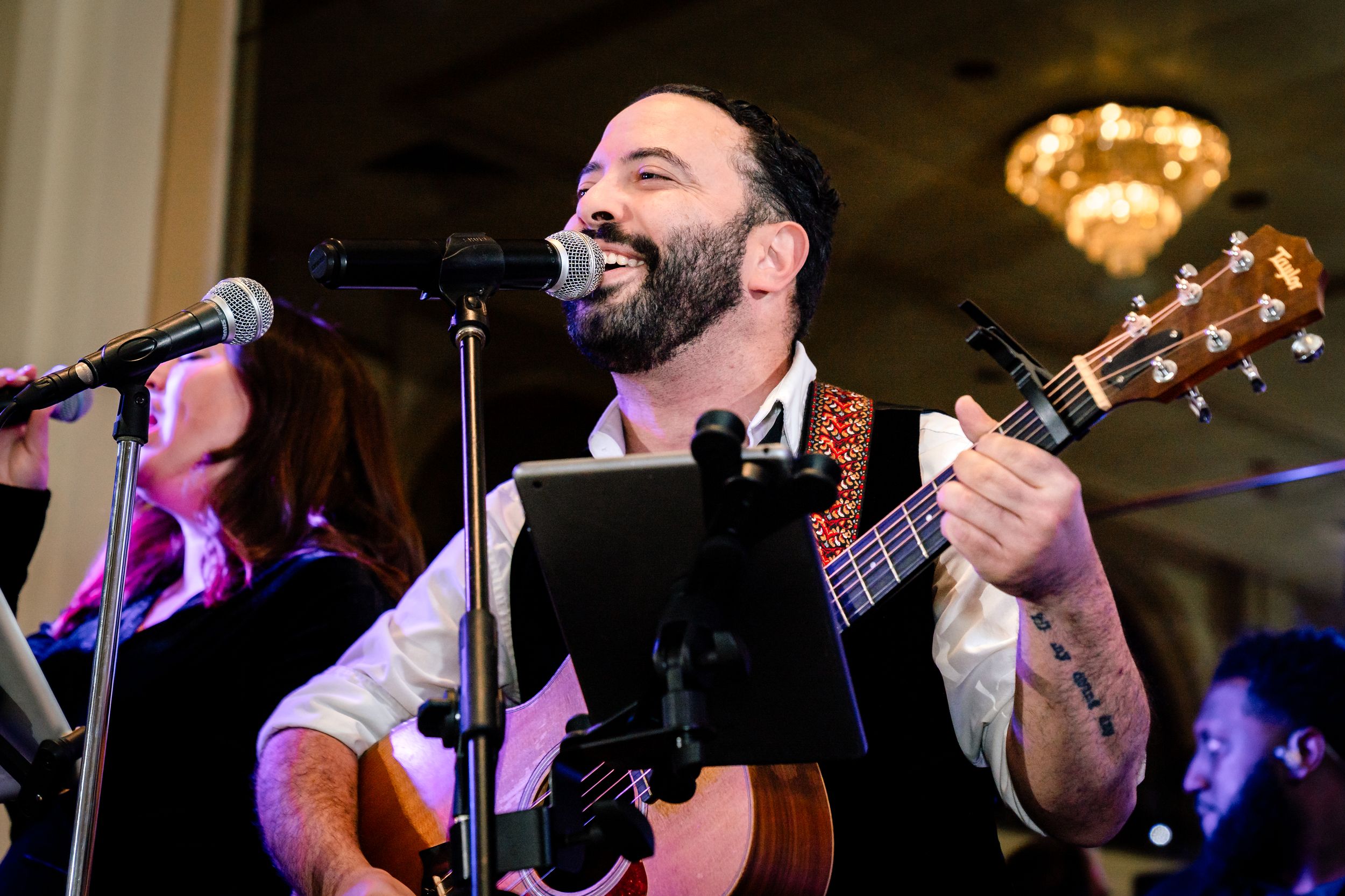 Musicians perform on stage with guitars and microphones during a live concert with colorful lighting.
