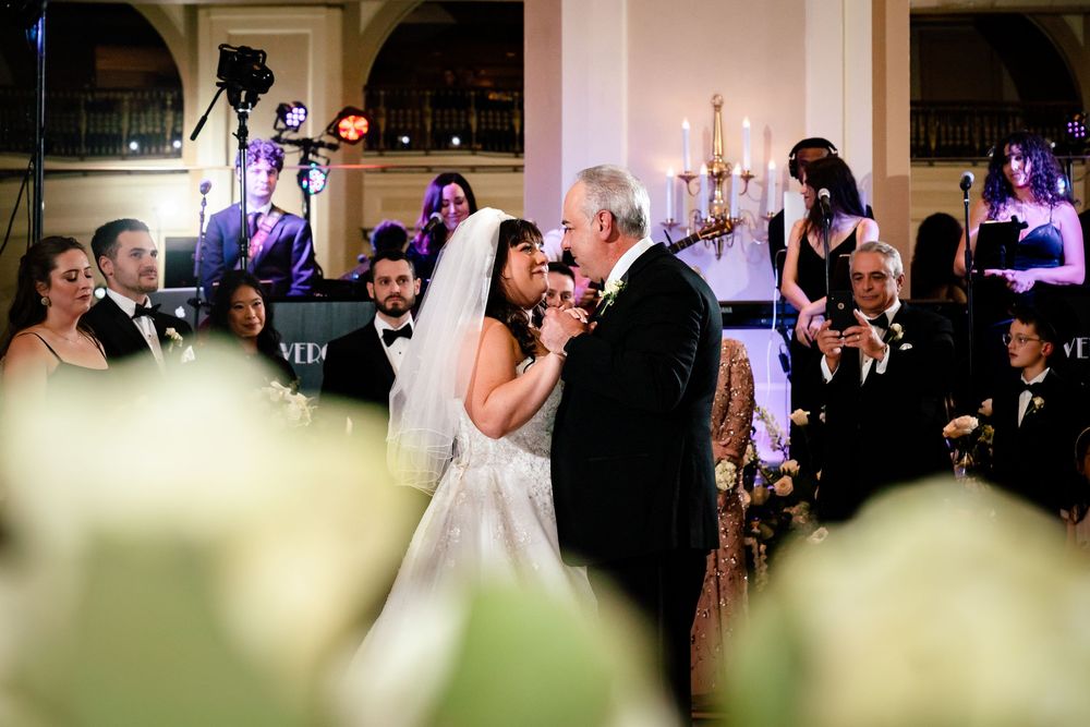 Wedding party dancing and celebrating in an elegant ballroom setting with soft lighting.