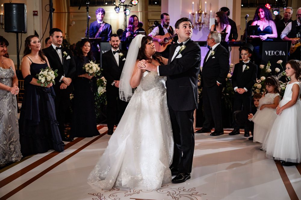 Wedding guests dance and celebrate on an elegant ballroom floor illuminated by purple lighting.