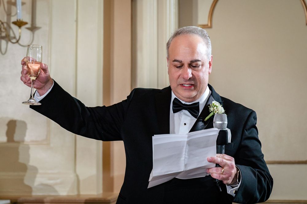A man in formal attire delivers a speech at an elegant wedding reception.