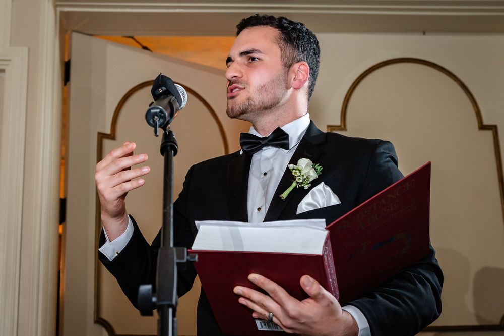 Groom reading from burgundy folder during wedding ceremony in elegant indoor venue.