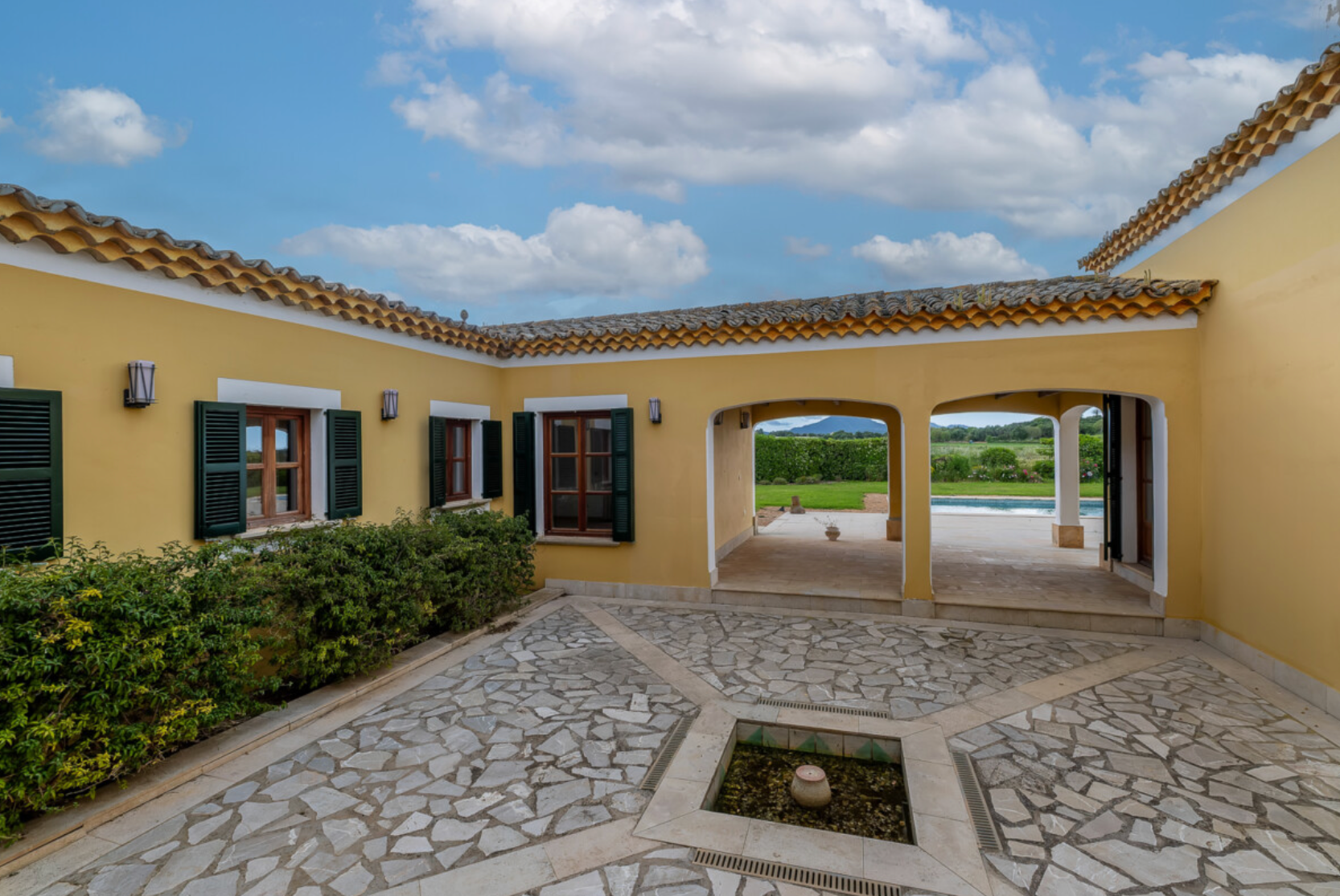 A panoramic view of a Mediterranean style villa with stone patio and covered walkways under bright blue skies.