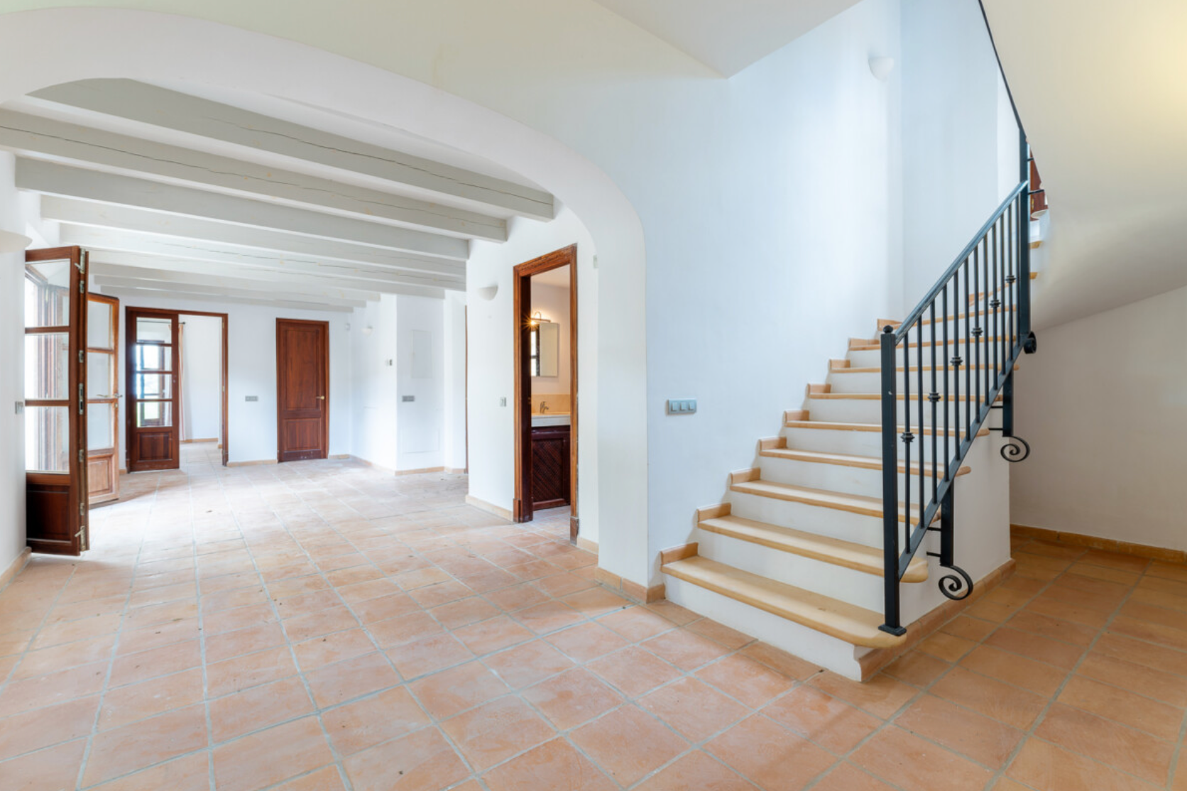 Modern interior hallway with white walls, wooden stairs, and black metal railing leading to upper level.